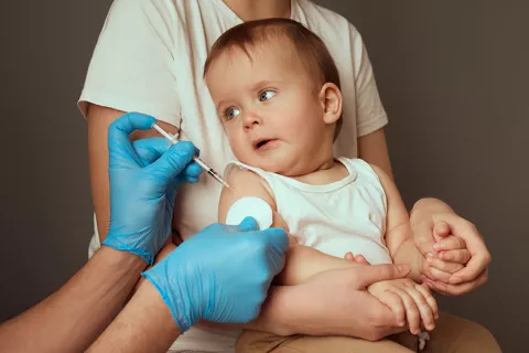 14 millones de bebés sin vacunas Cuidador sostiene a un niño pequeño en preparación para una vacunación