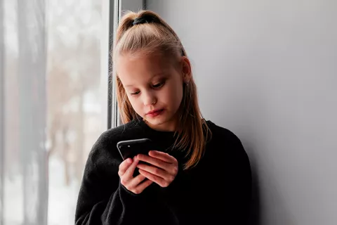 Niña rubia mira su teléfono inteligencia con cara de tristeza