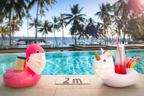 Verano y piscinas riesgo de criptosporidiosis Dos flotadores con mascarillas puestas y una piscina con palmeras de fondo