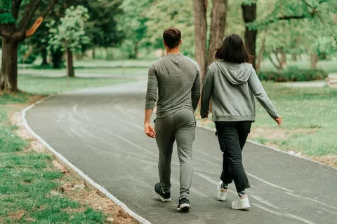 Objetivo de 7000 pasos diarios para mejorar la salud Una pareja en chándal camina de espaldas por un parque