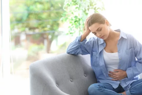 Mujer con dolor menstrual a causa de la endometriosis Mujer joven sentada en un sofá se toca el vientre dolorido