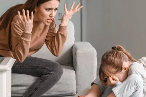Madre grita a su hija que está sentada en el suelo tapándose la cara