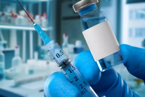 Mano de un investigador sostiene un vial de vacuna experimental y una jeringuilla