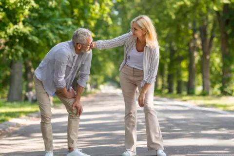 Hombre maduro se toca la rodilla dolorida mientras camina por el parque con su pareja
