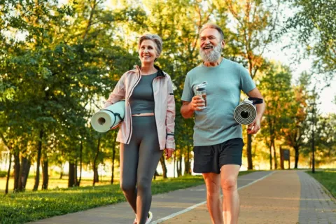 Una mujer y un hombre mayores se disponen a hacer ejercicio al aire libre Pareja de adultos mayores camina por un parque con útiles para hacer deporte