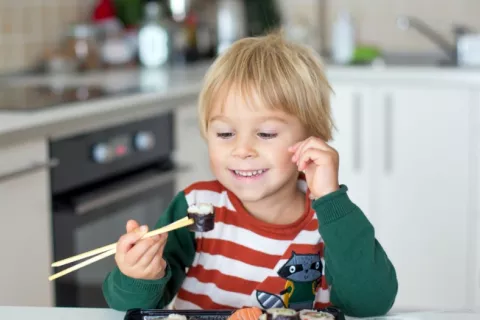 Un niño sonriente se dispone a comer un plato de sushi en la cocina de su casa