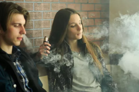 Un chico y una chica adolescentes vapean en el interior de un edificio