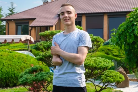 Chico joven con brazo derecho amputado sonríe a la cámara en el jardín de su casa
