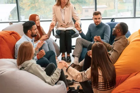 Grupo de jóvenes asisten a terapia para mejorar su salud mental Grupo de jóvenes sentados en círculo alrededor de su terapeuta cogidos de la mano