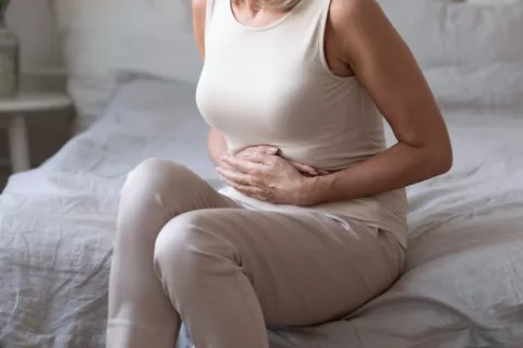Mujer de mediana edad sufre de trastornos digestivos Mujer de mediana en la edad sentada en la cama con las manos en el abdomen dolorido