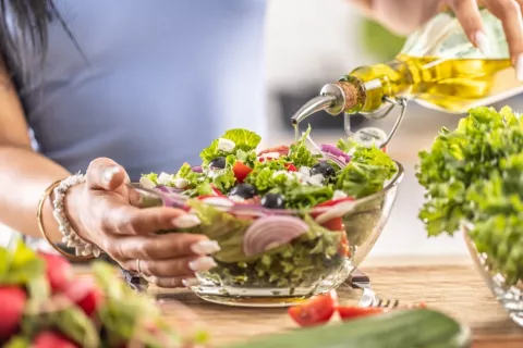 Dieta mediterránea, aceite de oliva y riesgo de diabetes Mujer echando aceite de oliva a una ensalada mediterránea