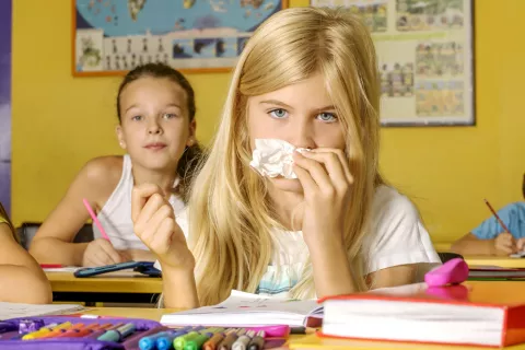 Vuelta al cole para niños alérgicos y asmáticos Niña en el colegio se suena los mocos con un pañuelo