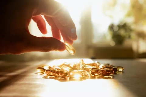 Suplementos de vida D frente al envejecimiento Una mano cogiendo suplementos de vitamina D iluminados por el sol