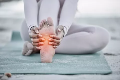 Dolor en los pies vinculado a la fibromialgia Mujer se duele de un pie sentada sobre una esterilla
