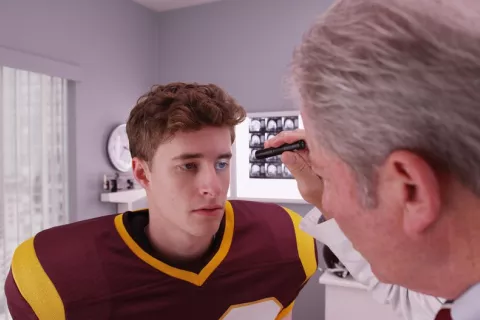 Efectos de traumatismos craneoencefálicos en atletas jóvenes Jugador de fútbol americano siendo explorado por el neurólogo