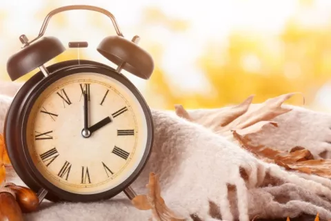 Reloj despertador junto a manta y hojas otoñales