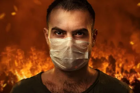 Hombre se protege con una máscara con un incendio forestal a su espalda