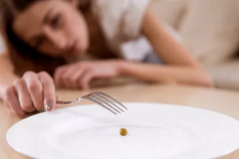Chica joven con malnutrición muy delgada Joven muy delgada a punto de pinchar un guisante de un plato