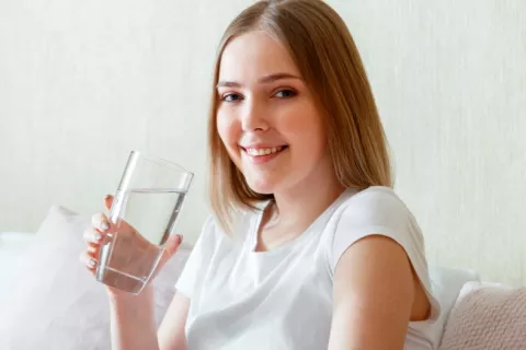 Chica joven sonríe a la cámara sosteniendo un vaso de agua