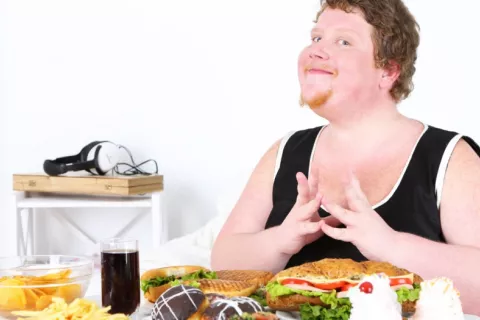 Hombre obeso sentado a una mesa repleta de alimentos