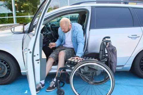 Hombre con discapacidad en el acto de pasar de su coche a su silla de ruedas