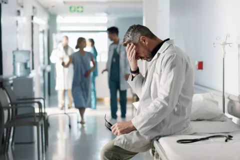 Profesional sanitario con gesto de abatimiento durante su jornada laboral Médico sentado sobre una camilla se toca la frente con gesto abatido