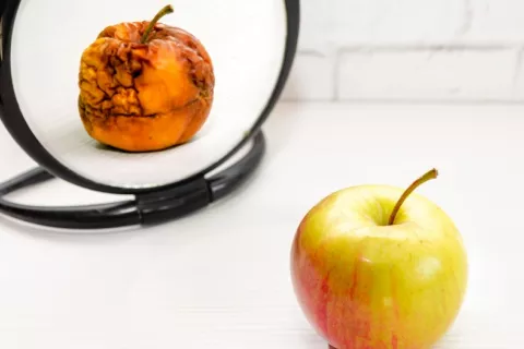 Manzana sana frente a espejo donde se ve el reflejo de una manzana pocha y arrugada