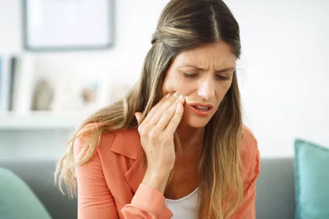 Mujer se toca un lado de la mandíbula con gesto de dolor