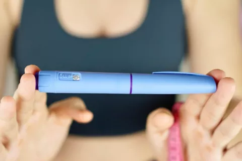 Mujer muestra una pluma de Ozempic y una cinta métrica Una mujer con ropa deportiva sujeta una pluma con semaglutida
