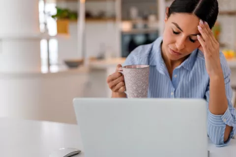 A una mujer con una taza de café le cuesta prestar atención a la pantalla de su ordenador Mujer con aspecto cansado sostiene una taza de café frente a su portátil
