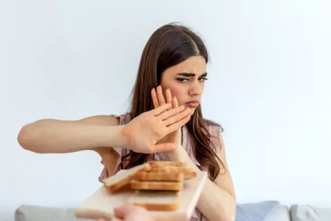 Mujer joven rechaza rebanadas de pan con gesto preocupado Una joven hace gesto de rechazo cuando le ofrecen rebanadas de pan