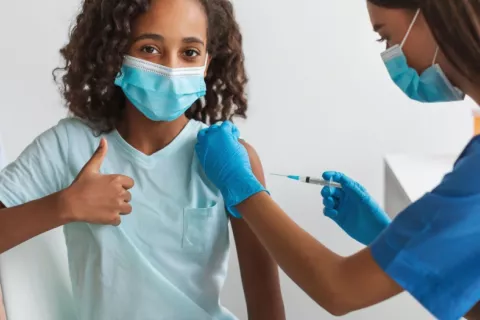 Sanitaria vacunando a una niña contra el COVID-19 Niña hace un gesto de aprobación con el pulgar mientras es vacunada