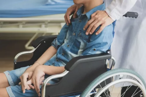 Niño en silla de ruedas con distrofia muscular atendido por un médico Médico apoya sus manos sobre un niño en silla de ruedas con problemas musculares