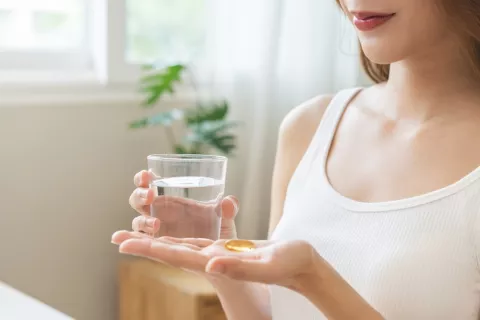Mujer joven en camiseta de tirantes sostiene un vaso y una vitamina D en la otra mano
