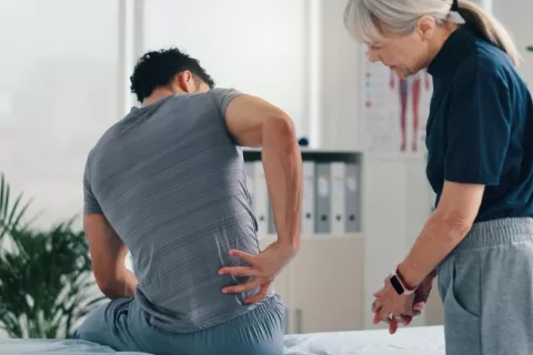 Hombre joven acude a una fisioterapeuta por sufrir lumbalgia Hombre joven con dolor lumbar en la consulta de una fisioterapeuta