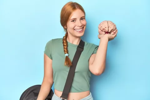 Entrenar nos ayuda a fortalecer el cerebro Mujer joven con bolsa de entrenamiento sostiene un cerebro de plástico sonriendo