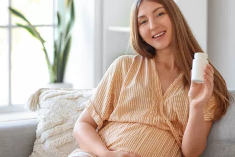 Joven embarazada muestra sonriente un frasco de vitaminas
