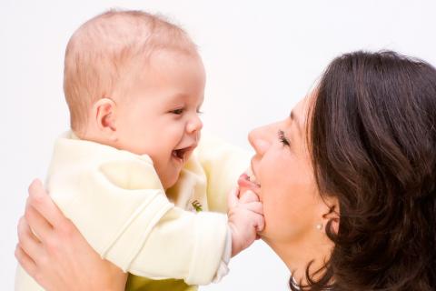 Una madre levanta a su bebé en brazos, sonriéndole mientras él le toca la cara