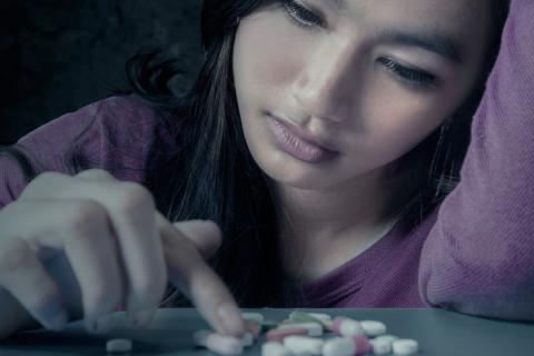 Una adolescente contempla un montón de pastillas sobre una mesa