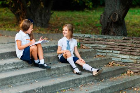 Dos niñas con uniforme escolar charlan en un parque