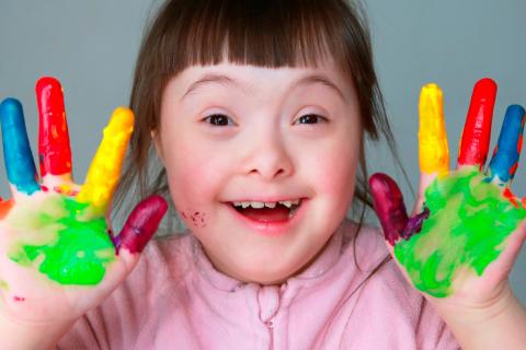 Niña con Síndrome de Down con las manos pintadas y feliz
