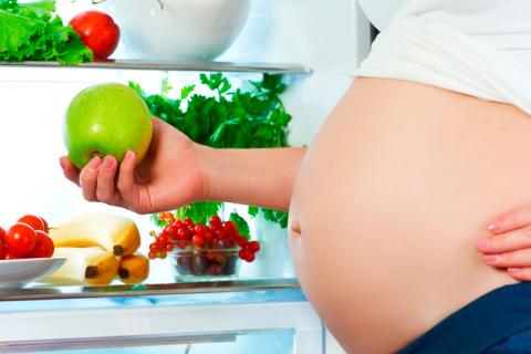 Mujer embarazada cogiendo una manzana del frigorífico