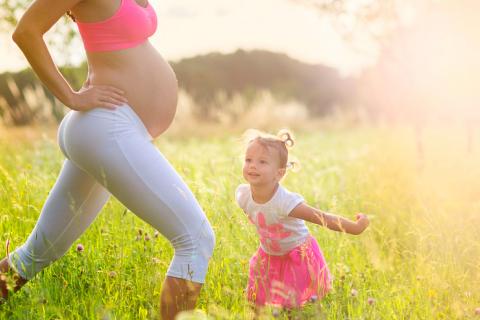 Mujer embarazada realizando ejercicio aeróbico con su hija pequeña