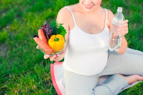 Una embarazada sostiene unas verduras y una botella de agua