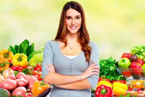 Mujer posa delante de un puesto lleno de frutas y verduras