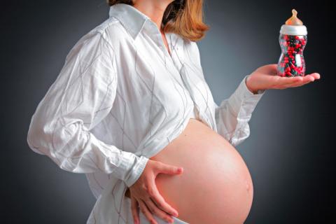 Mujer embarazada sujeta un biberón lleno de cápsulas 