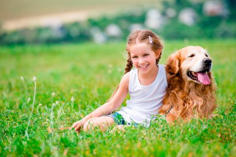 Niña sonríe sentada junto a su perro en el campo
