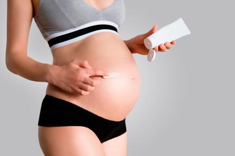 Una mujer embarazada se aplica una crema sobre la barriga