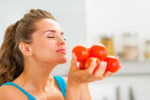 Una mujer aspira el aroma de tomates que sostiene en sus manos