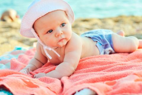 Bebé tumbado sobre una toalla en la playa con un gorrito en la cabeza